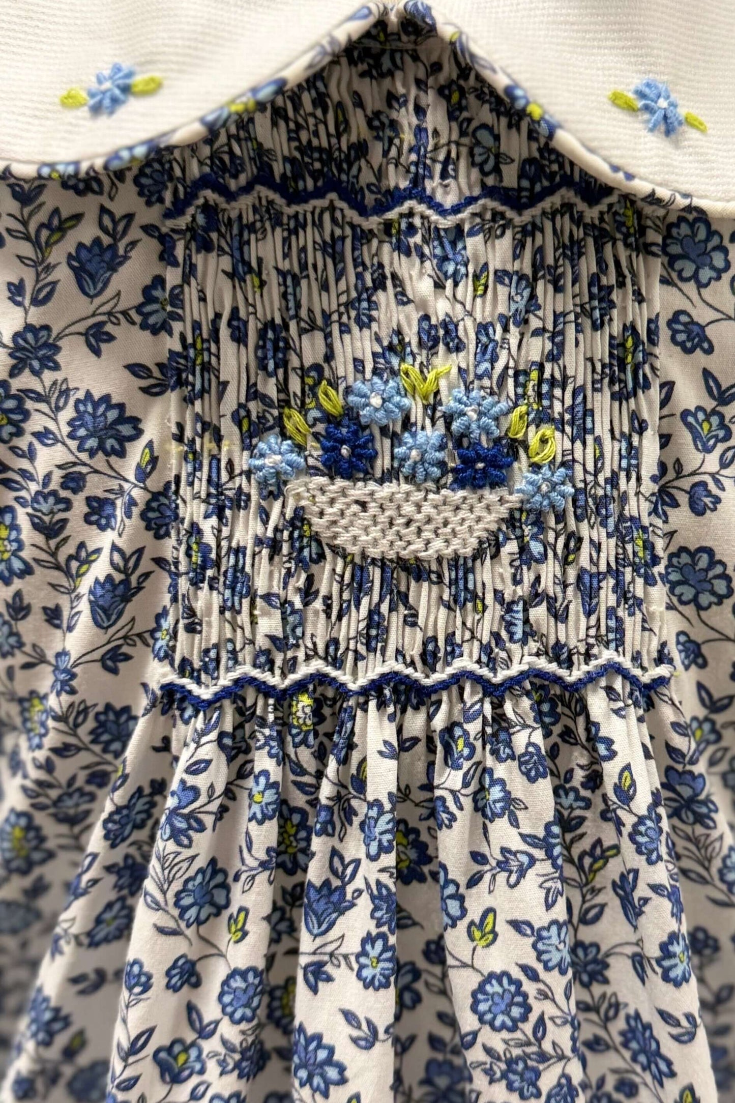 Close-up of floral fabric with hand-smocking and flower basket embroidery on a blue dress.