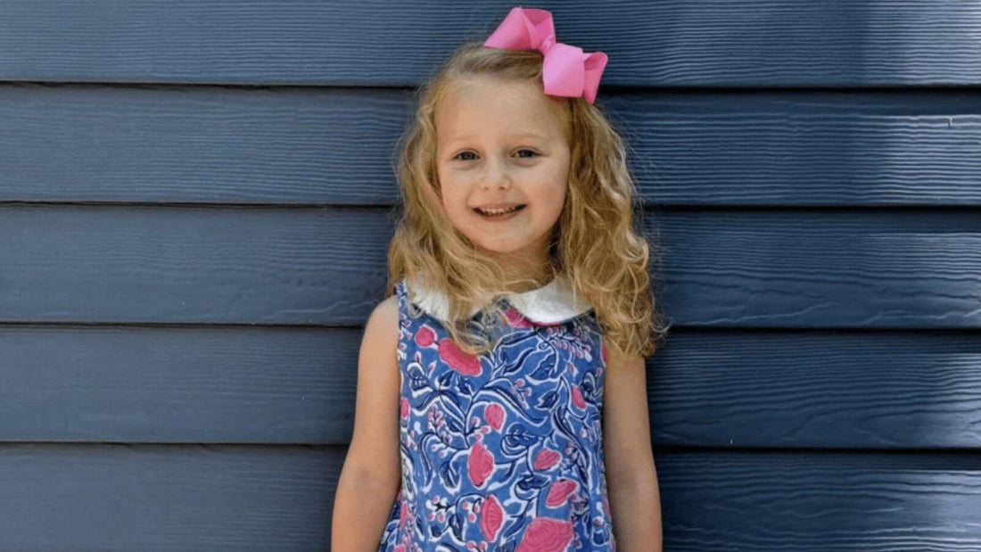 Little girl in Sky and Pink Floral Dress with a big smile standing against a navy blue wooden wall.