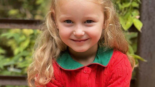 Little girl wearing Emily Lacey's red cotton cable knit cardigan, smiling outdoors.