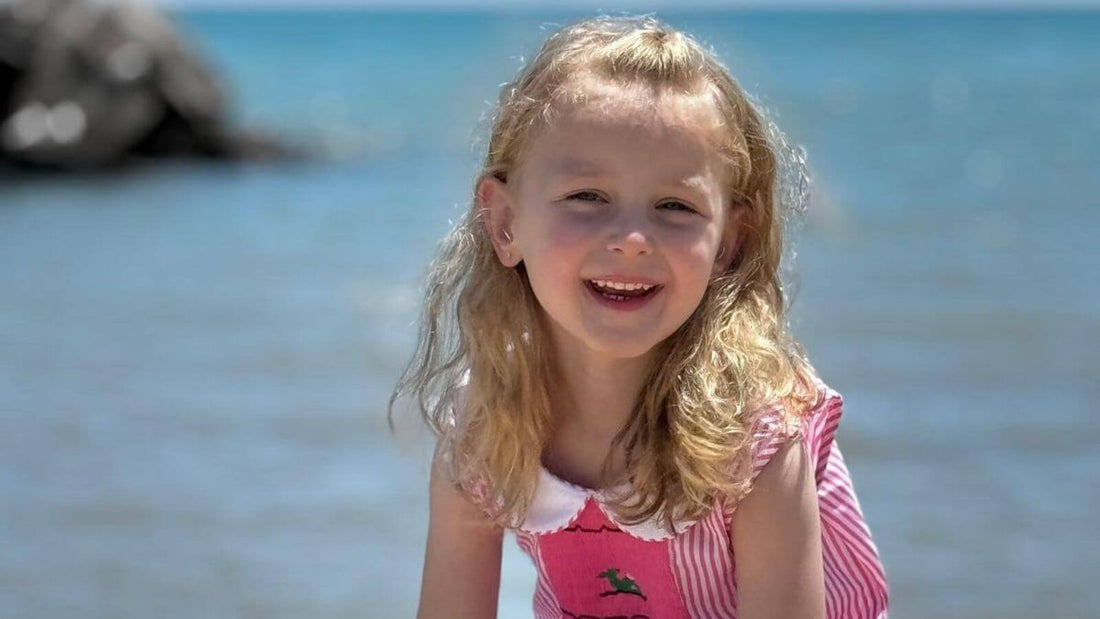 Little girl wearing a smocked whale dress, smiling by the beach. Discover style, comfort, and craftsmanship with Emily Lacey's children's fashion.