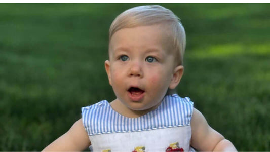 Toddler wearing Smocked Firetruck John John in a green outdoor setting