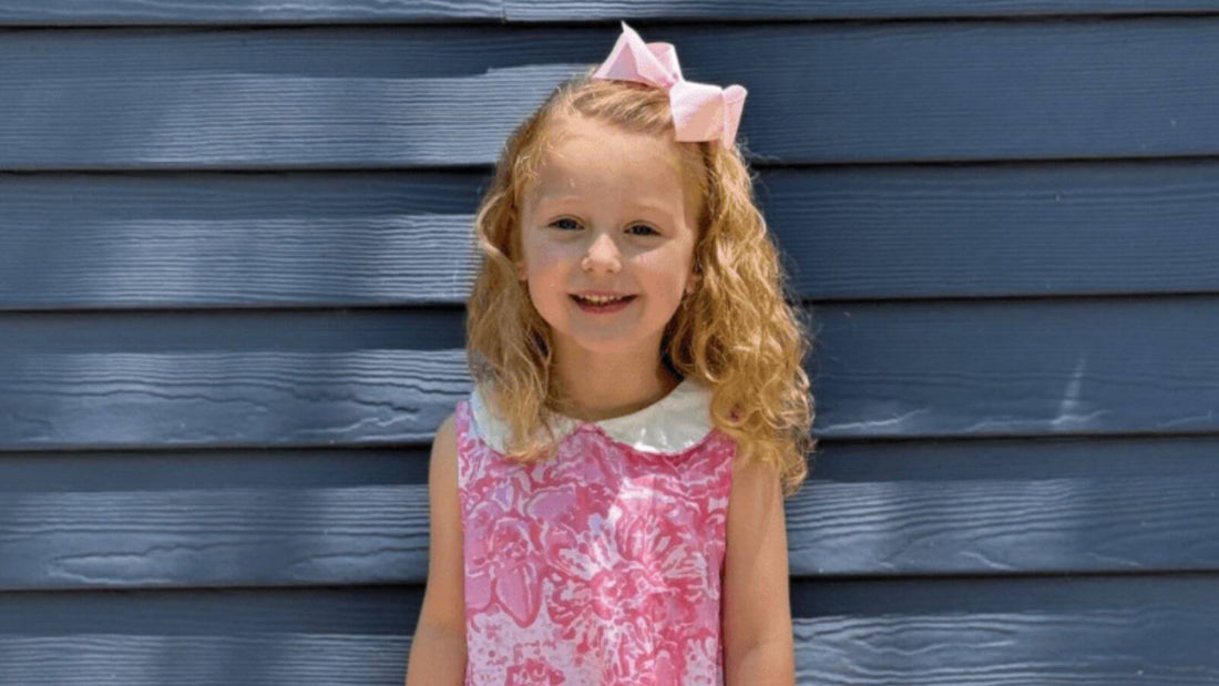 Little girl smiling in a pink watercolor dress with a matching bow, ready for the new school year.