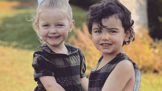 Two happy children wearing stylish smocked macro check dresses, enjoying a sunny day outdoors with smiles.