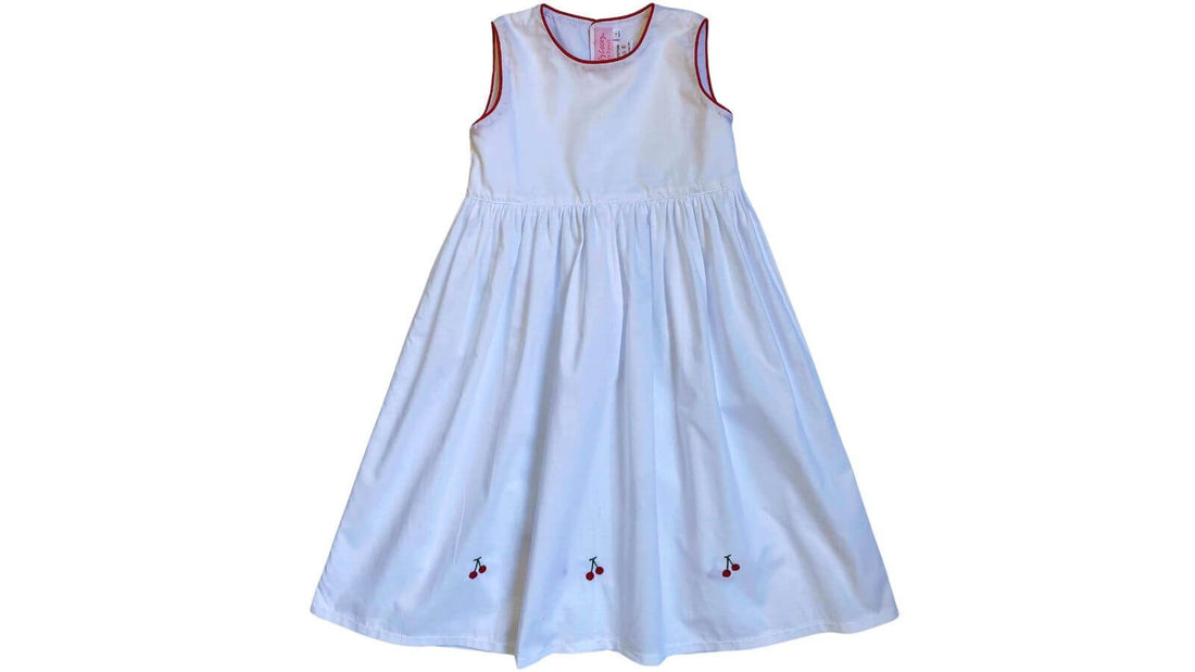 Smocked White Cherry Dress by Emily Lacey, perfect summer attire featuring delicate cherry embroidery – capture childhood's sunshine and laughter.