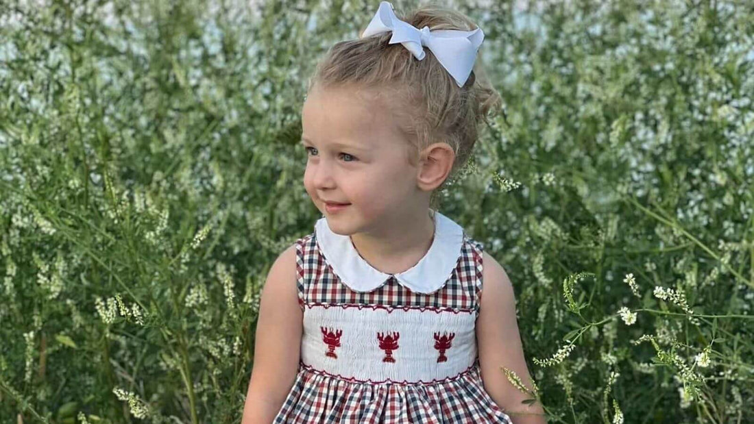 Little girl in a smocked lobster dress enjoying a sunny day in a field of greenery.