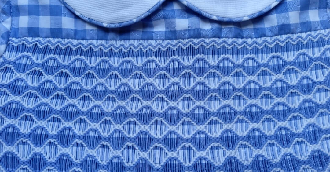 Close-up of hand-smocked blue gingham fabric showcasing intricate detailing perfect for spring fashion.