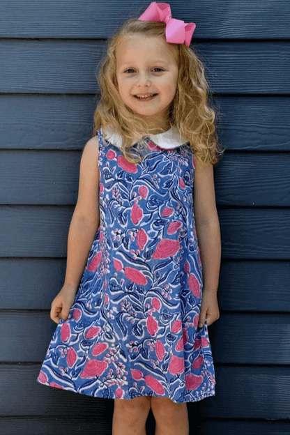 Girl wearing a charming Sky and Pink Floral Dress with an elegant A-line cut, standing against a blue wall and smiling.