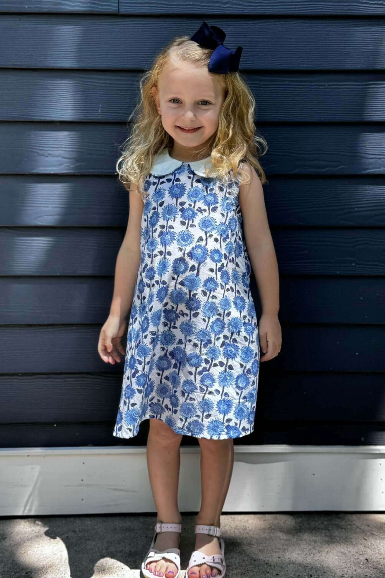 Little girl wearing a timeless Blue Sunflower Floral Dress, ready for school with a charming blue and white floral pattern.