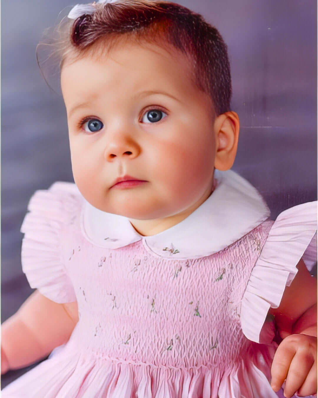 Adorable baby in pink smocked dress with ruffled sleeves and white collar, perfect for special occasions.