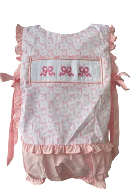 Hand-smocked bow set featuring pink fabric, embroidery, ruffles, and side ties for a sweet, artisanal look.