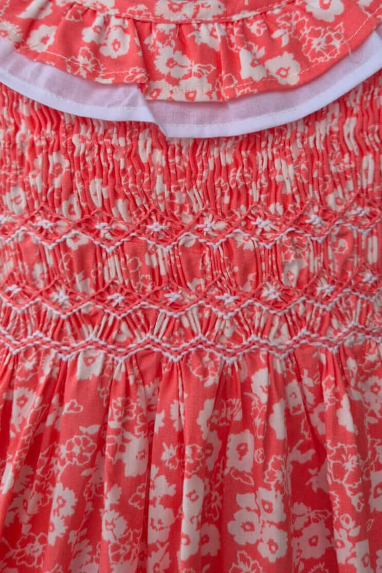 Close-up of hand-smocked coral floral dress featuring ruffle collar and delicate cotton print.