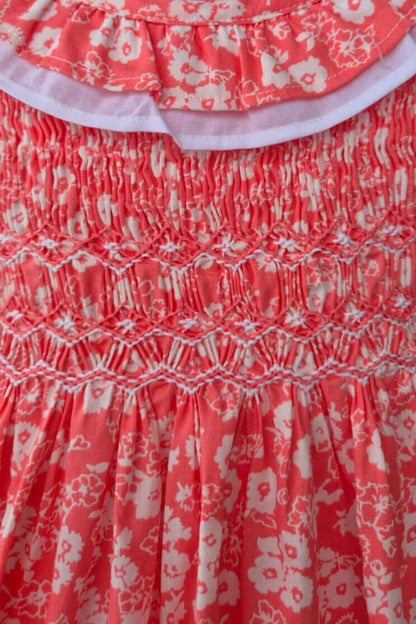 Close-up of hand-smocked coral floral dress featuring ruffle collar and delicate cotton print.