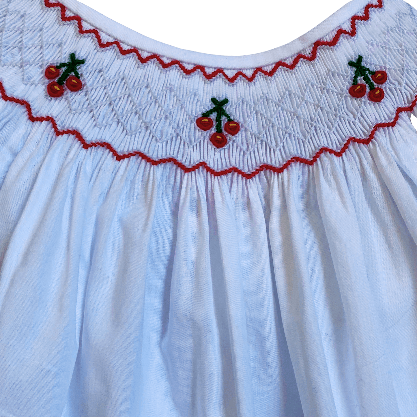 Close-up of hand-smocked cherry bishop dress with detailed cherry embroidery at the neckline and delicate floral pattern.