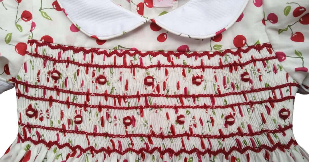 Close-up of hand-smocked cherry dress featuring a sweet cherry print and delicate red smocking, perfect for spring.