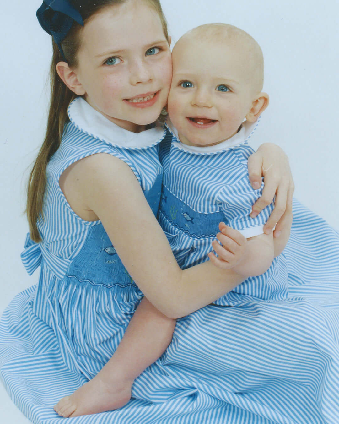 Two children in matching blue striped outfits, smiling and embracing for a heartwarming moment.