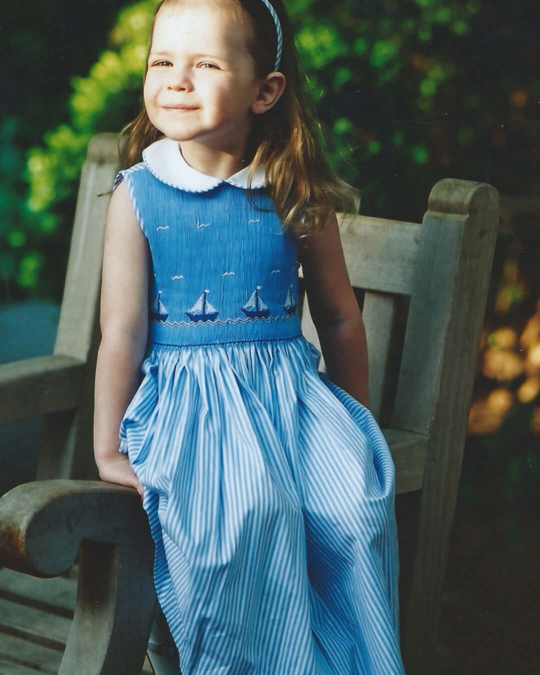 Smocked Sailboat Dress on young girl, featuring blue stripes and embroidered sailboats, perfect for summer outings.