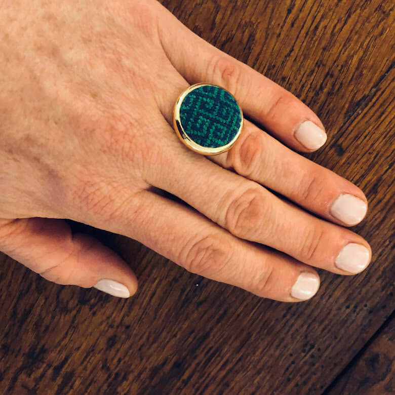 Hand wearing a Navy & Kelly Greek Key Needlepoint Ring featuring a unique green design on a gold band.