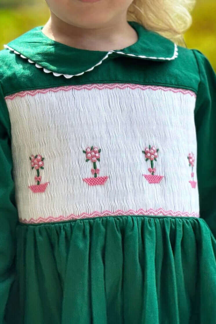 Little girl wearing a beautifully hand-smocked green topiary dress with intricate details, perfect for any special occasion.