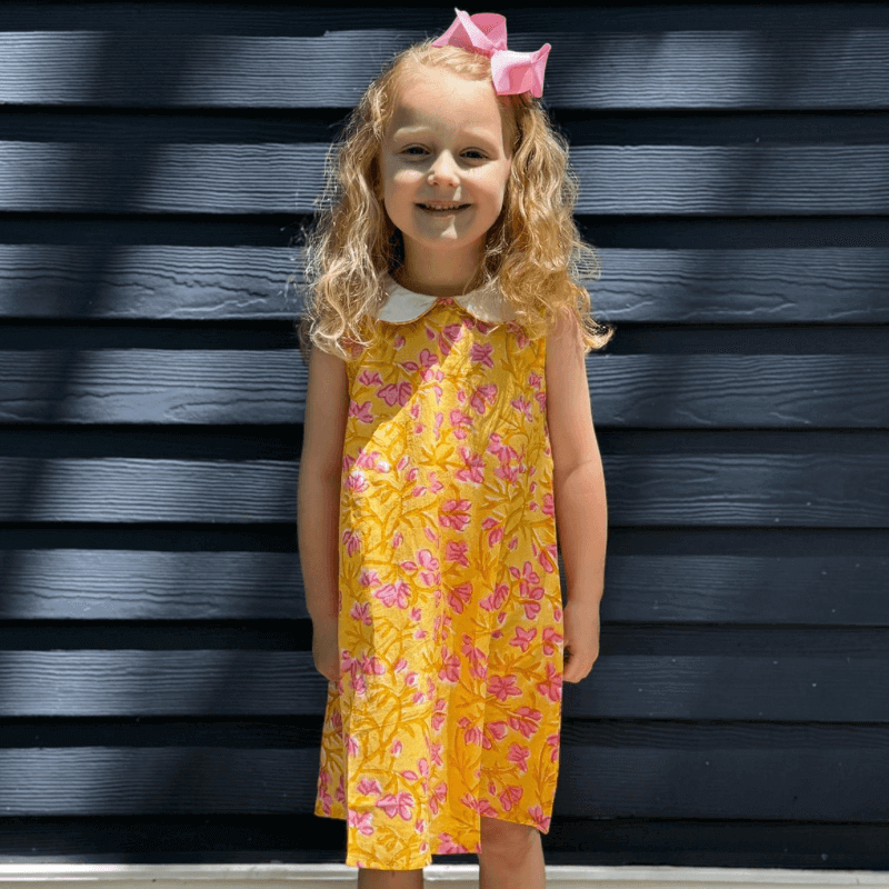 Young girl smiling in a sunny pink floral dress with Peter Pan collar and attached belt, perfect for back-to-school.