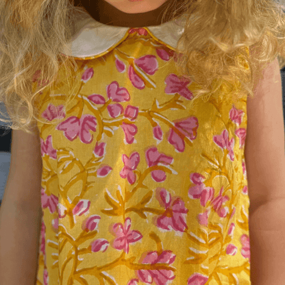 Little girl in a sunny floral dress with pink watercolor print, A-line cut, Peter Pan collar, and button back. Perfect back to school outfit!