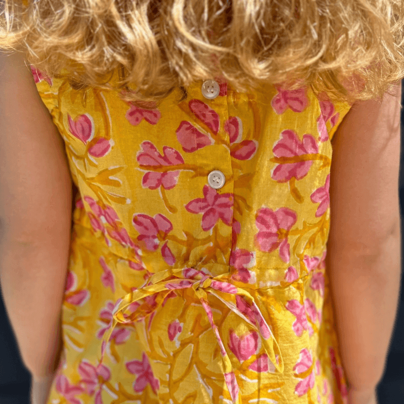 Girl wearing Sunny Floral Dress with pink watercolor print, Peter Pan collar, button back, and attached belt. Perfect for back to school.