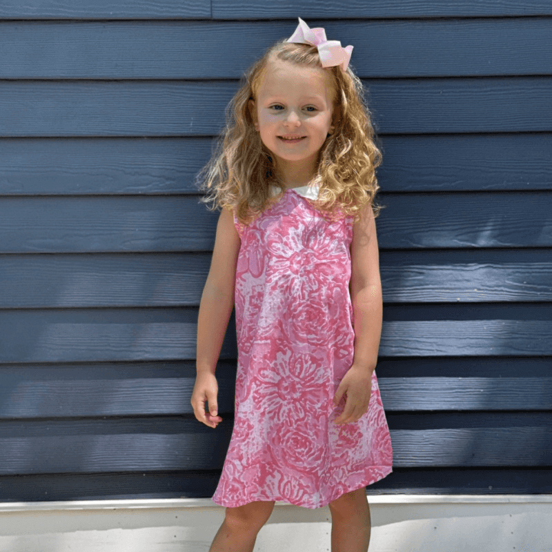 Little girl smiling in a pink watercolor Aline dress with Peter Pan collar and attached belt, perfect for back-to-school.