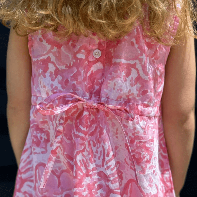 Girl wearing pink watercolor A-line dress with Peter Pan collar, button back, and attached belt, ready for a stylish back-to-school look