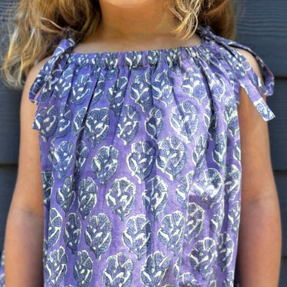 Little girl modeling a purple floral sun dress with watercolor print and sleeveless design, perfect for back-to-school fashion.