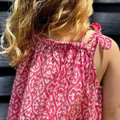 Girl in pink floral sun dress with watercolor print and shoulder bow details, perfect for back to school days.