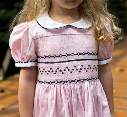 Little girl wearing a handcrafted smocked pink and navy geo dress with elegant ric rac trim.