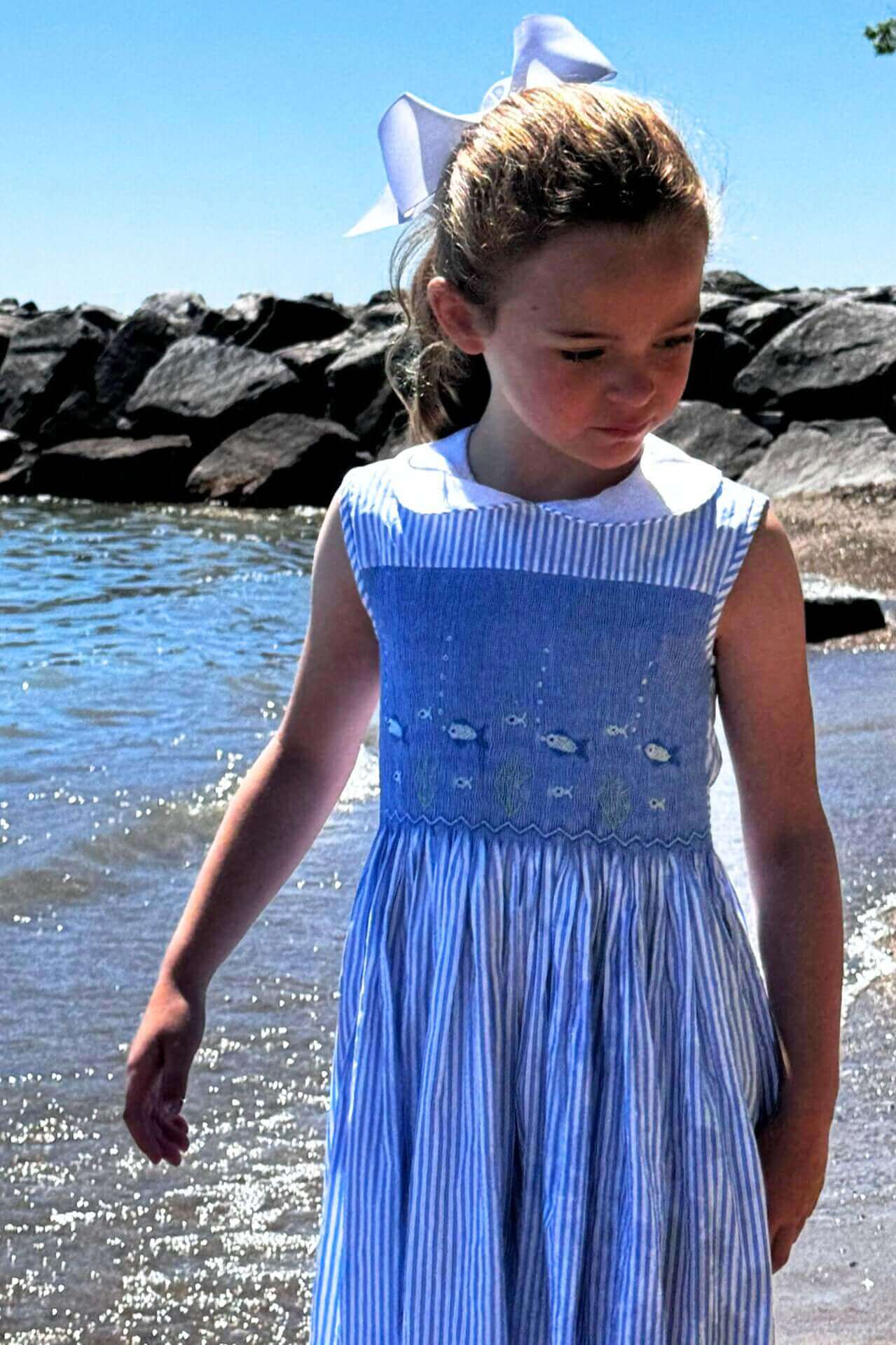 Girl in smocked fish dress enjoying a sunny beach day with a charming underwater scene on navy stripes.