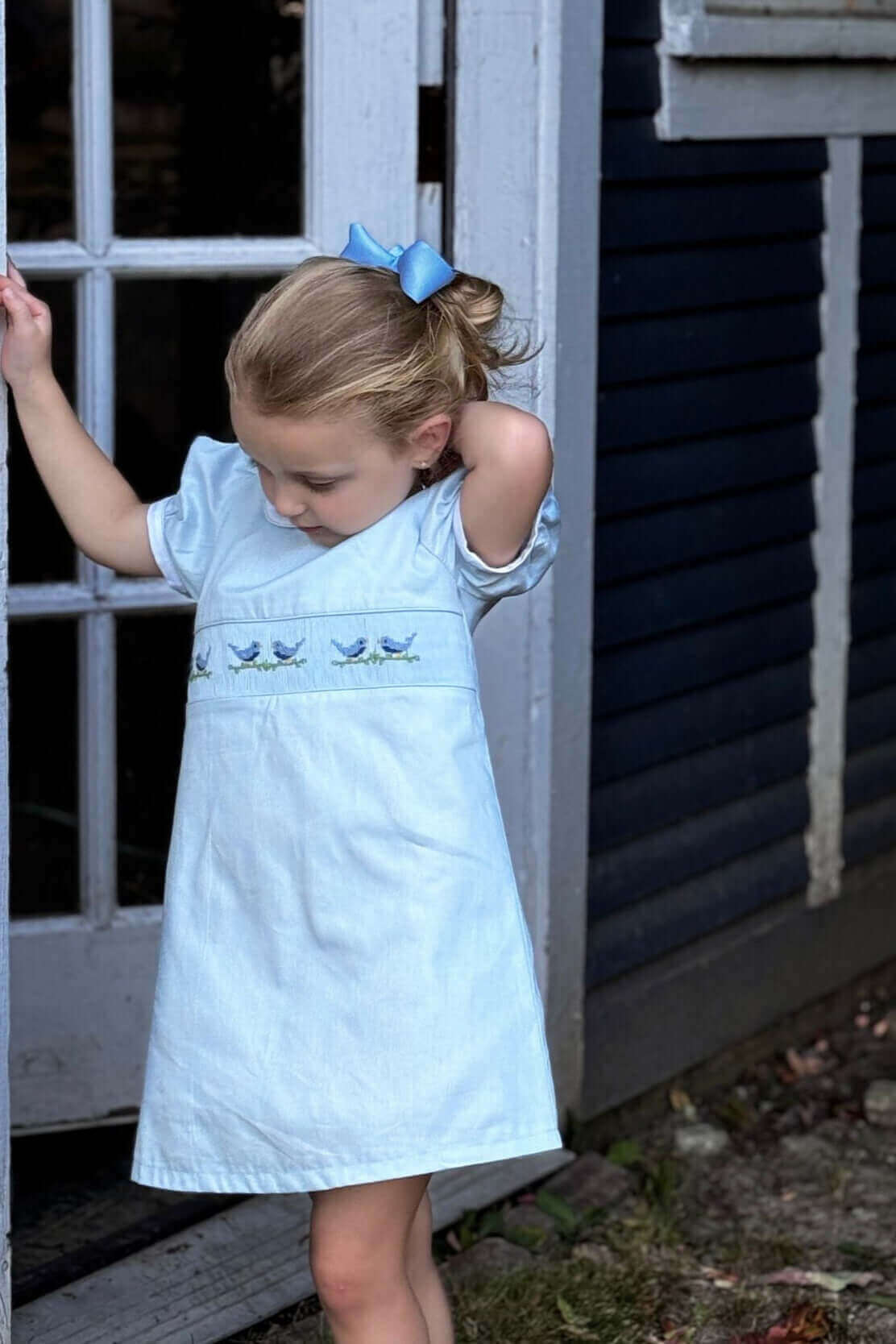 Little girl in a Smocked Sky Lovebird Dress with hand-smocked lovebird details, perfect for school photos, birthday celebrations, and daily wear.