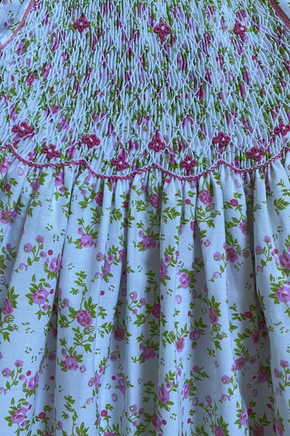 Close-up of a hand-smocked pink and green floral dress showcasing delicate floral embroidery.