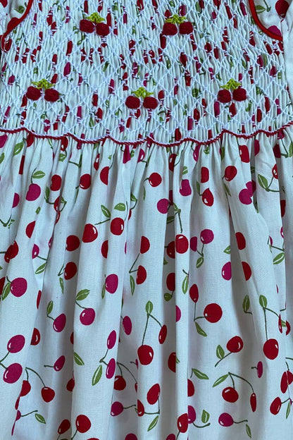 Hand-smocked cherry dress featuring delicate floral embroidery, perfect for stylish spring days.