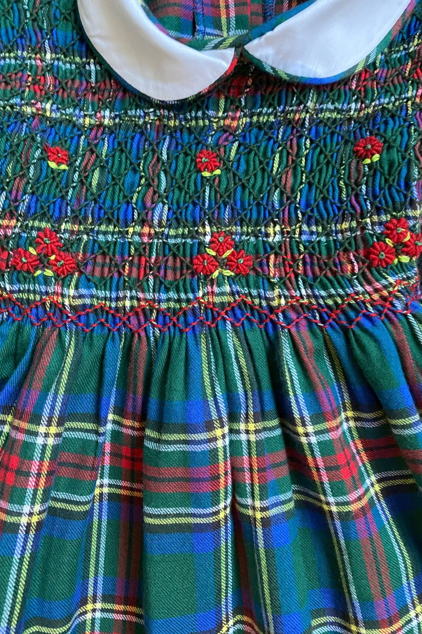 Close-up of a smocked flannel plaid dress featuring embroidered flowers and a white collar, perfect for special occasions.