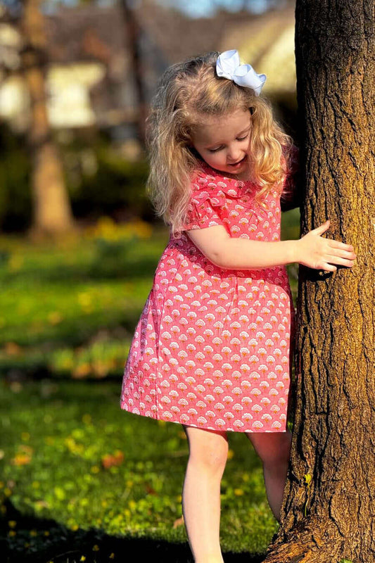 Little girl in Pinkberry Classic Dress next to a tree, showcasing floral print and Peter Pan collar, perfect for playful memories.