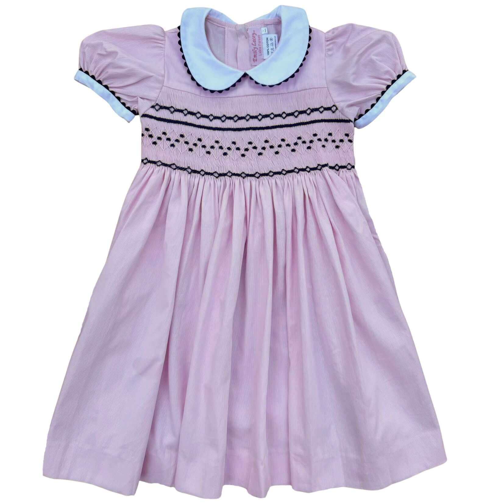 Smocked pink and navy geo dress with hand-smocked details, covered buttons, and ric rac trim, perfect for school photos and celebrations.