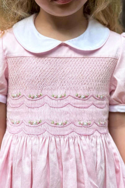 Little girl wearing elegant Smocked Pink Garland Dress, featuring hand-smocked details, covered buttons, and an attached belt for all occasions.