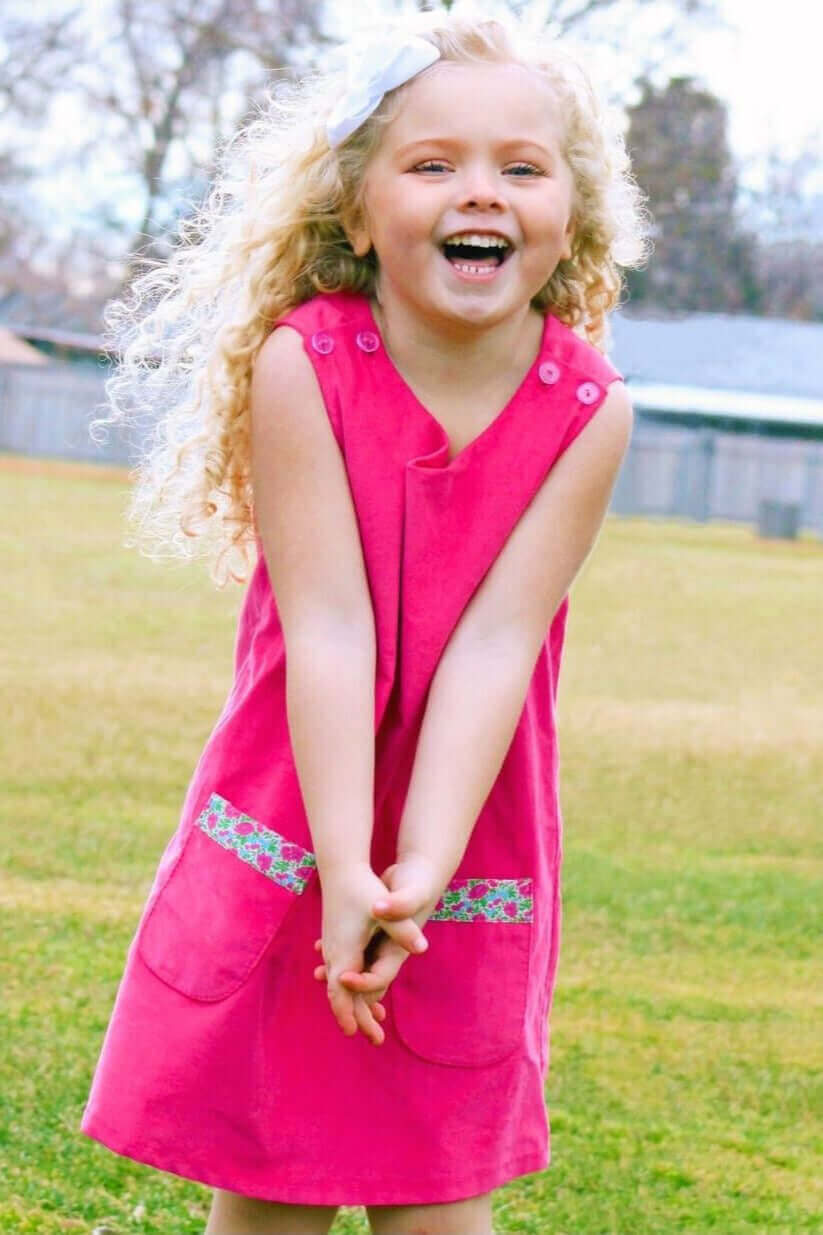 Little girl joyfully wearing a Liberty of London pink dress with trimmed pockets, perfect for stylish back-to-school wear.