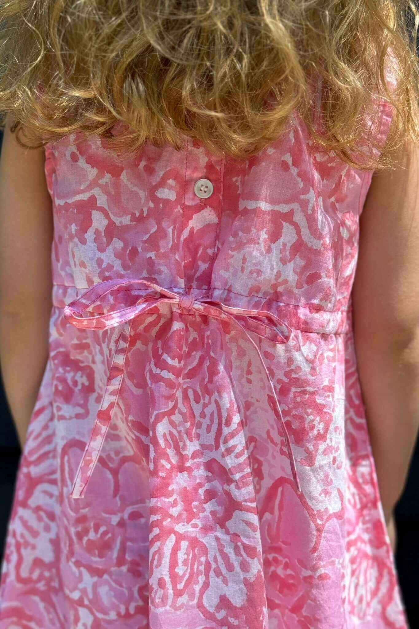 Young girl wearing a vibrant pink watercolor dress with a cute ribbon tie at the back, perfect for a standout school day outfit