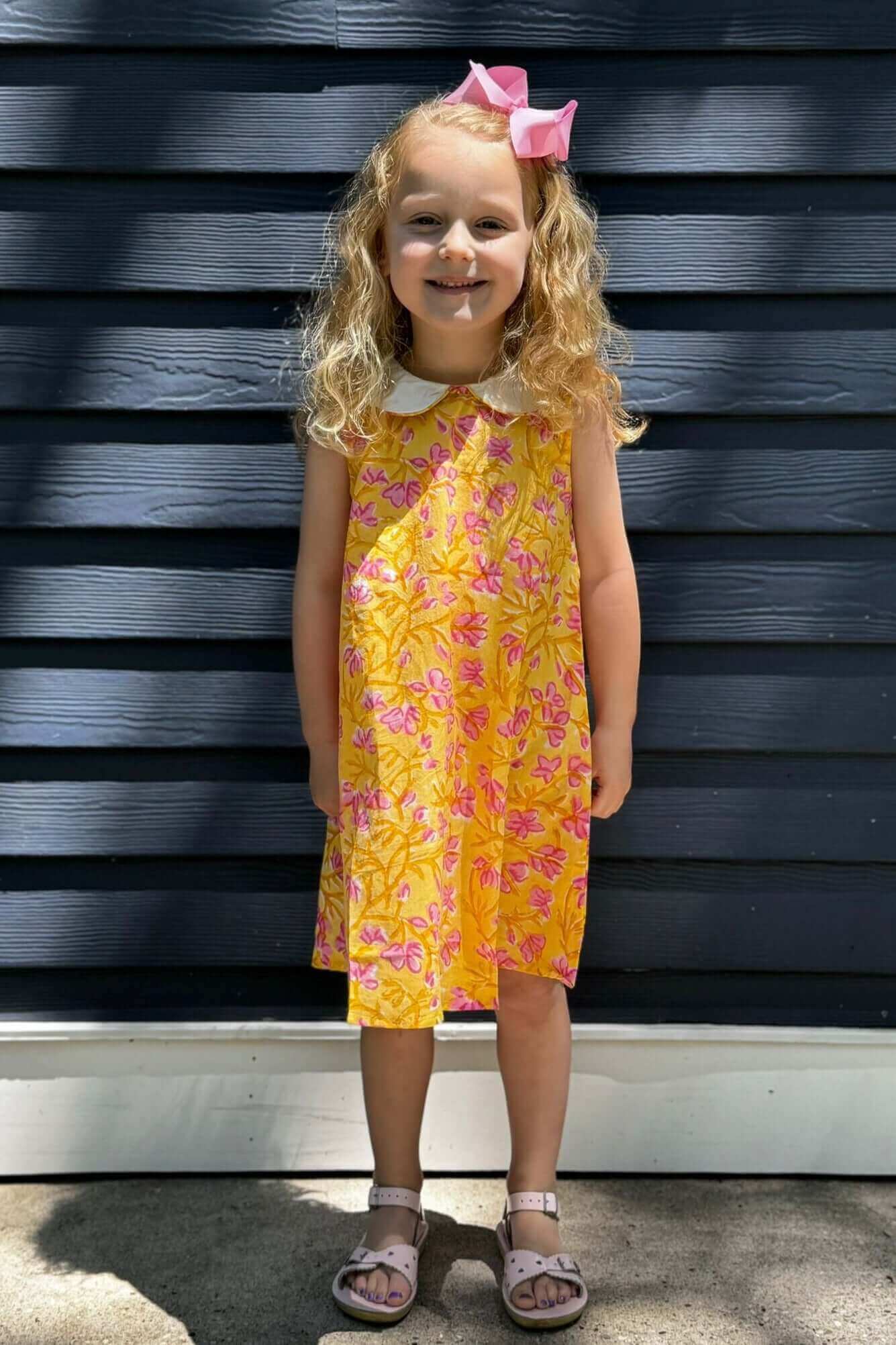 Little girl smiling in Sunny Floral Dress with a bright and cheerful floral print, ready for a delightful school day.