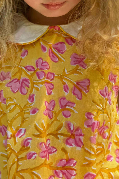 Girl wearing a Sunny Floral Dress with a vibrant yellow and pink floral pattern and elegant white collar.