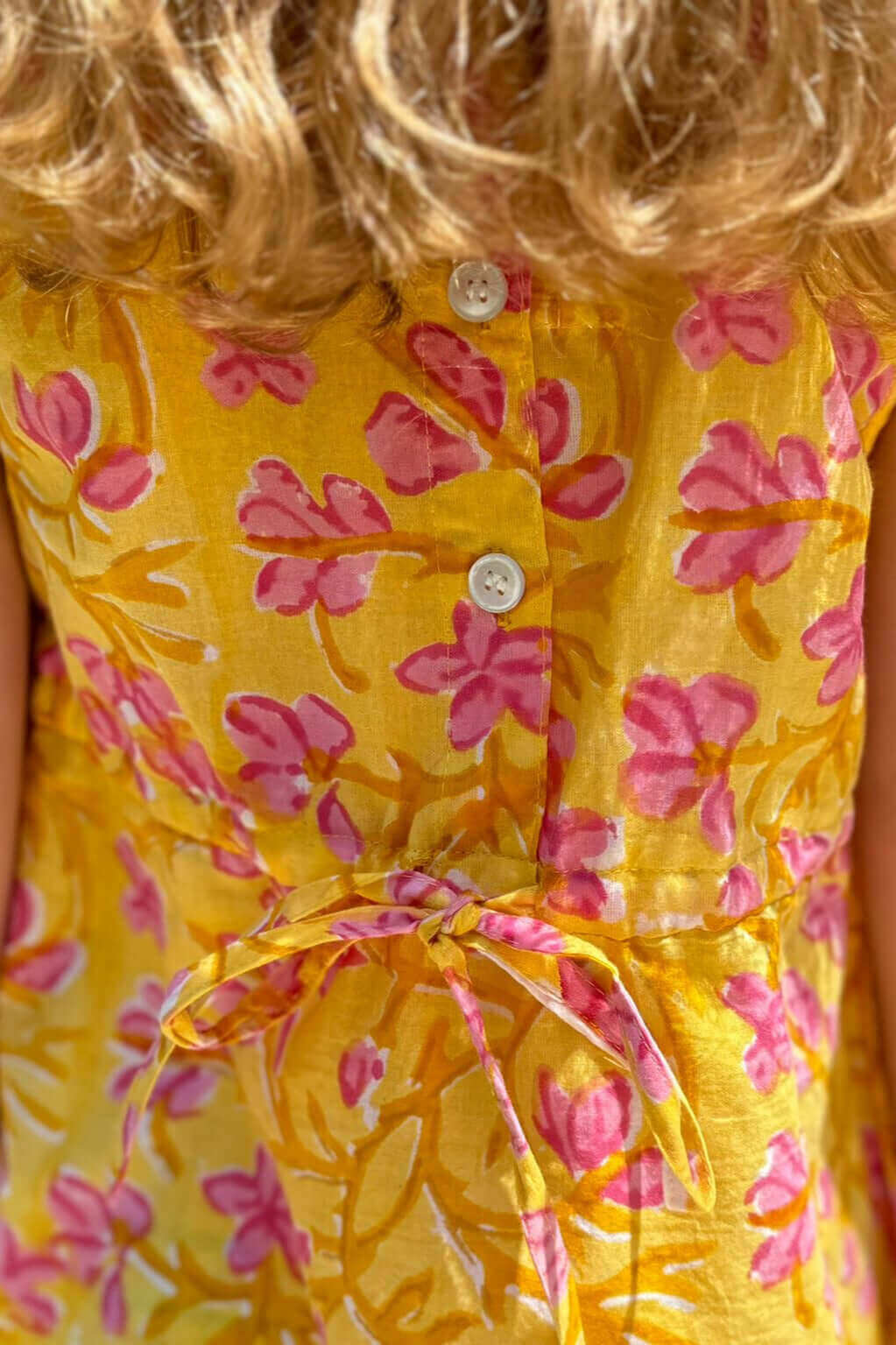 Close-up of Sunny Floral Dress with vibrant yellow and pink flowers, back buttons, and waist tie detail.