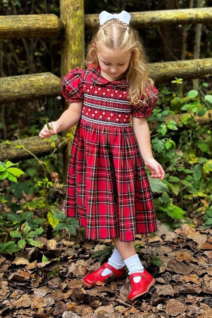 Little girl in a charming hand-smocked holiday plaid dress with covered buttons and attached belt, perfect for any festive occasion.