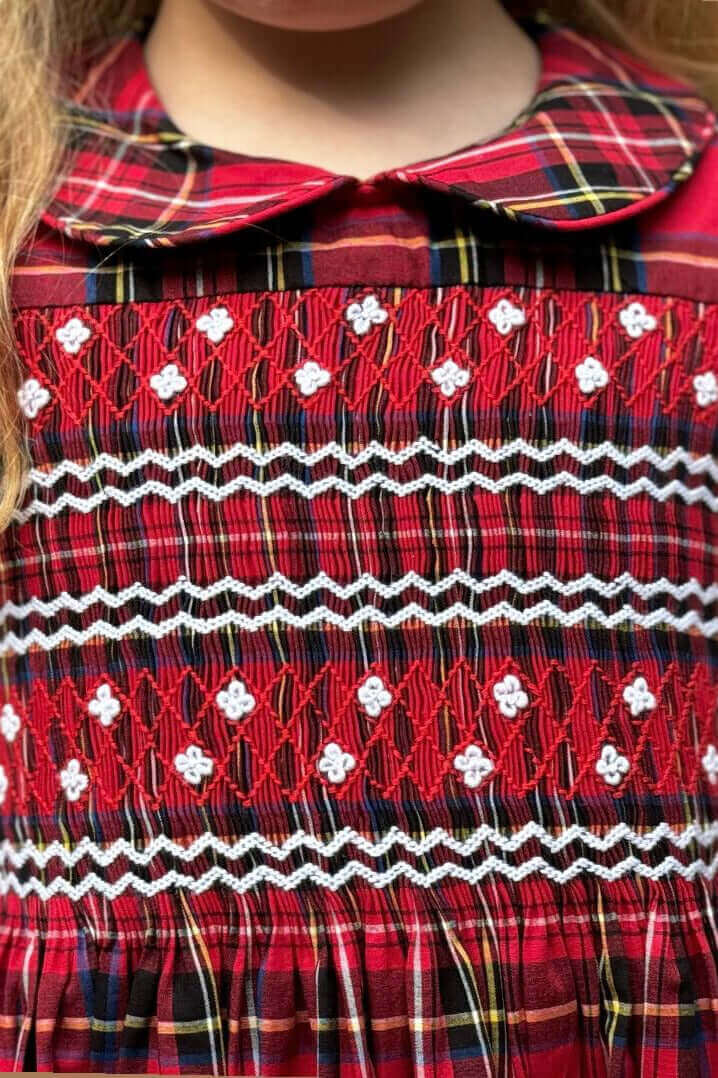 Close-up of a beautifully hand-smocked holiday plaid dress with intricate covered buttons and an attached belt, perfect for festive occasions.