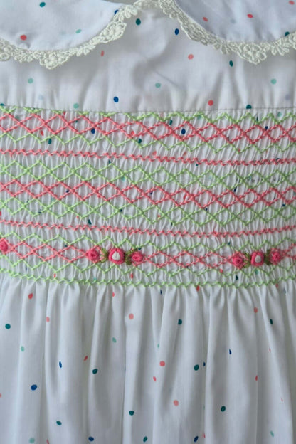 Close-up of a hand-smocked dress bodice featuring colorful embroidery on a white polka dot fabric.