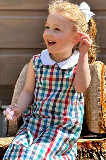 Young girl smiling in a classic preppy plaid dress with a white collar, holding flowers, showcasing timeless style and comfort.