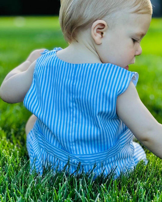 Cute baby wearing a classic smocked sailboat John John in blue stripes, sitting in green grass.