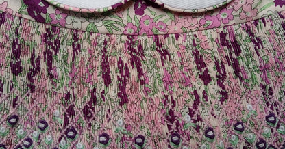 Close-up of hand-smocked violet floral dress showcasing intricate stitch patterns and vibrant colors.