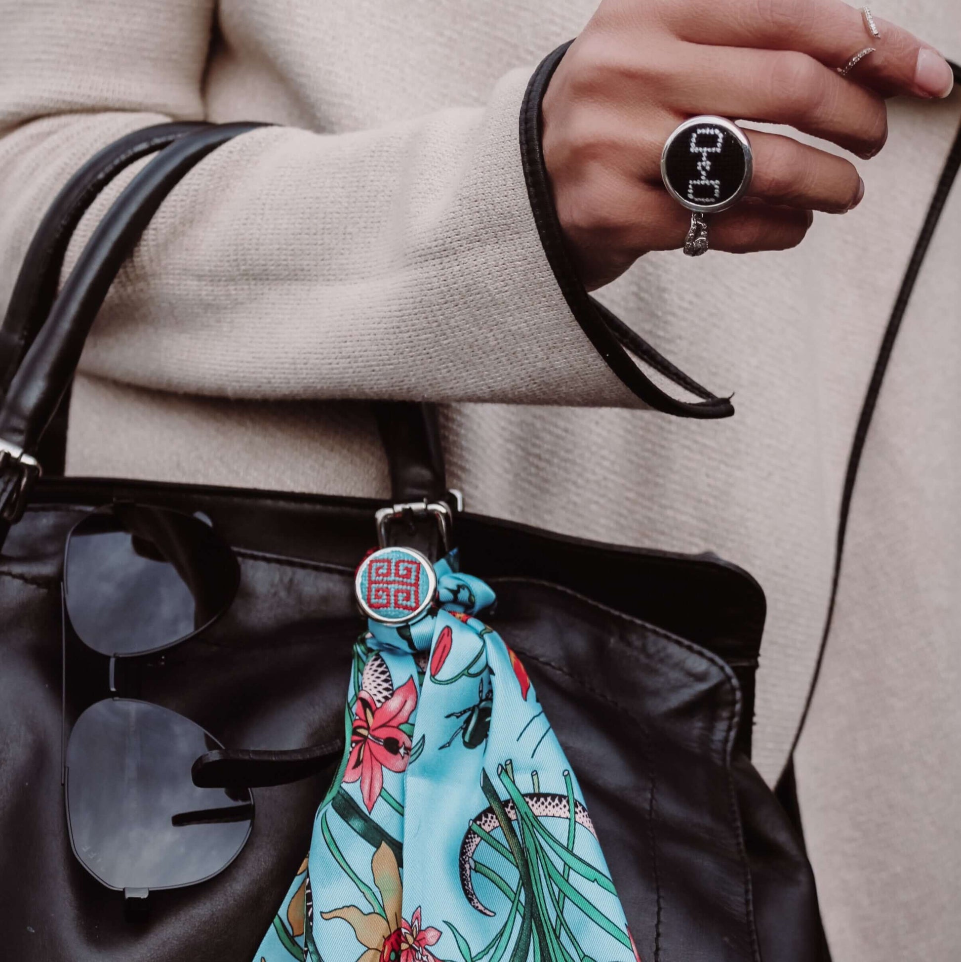 Stylish woman wearing a Blue and Red Greek Key Needlepoint Ring, holding a black handbag with a vibrant scarf accessory.